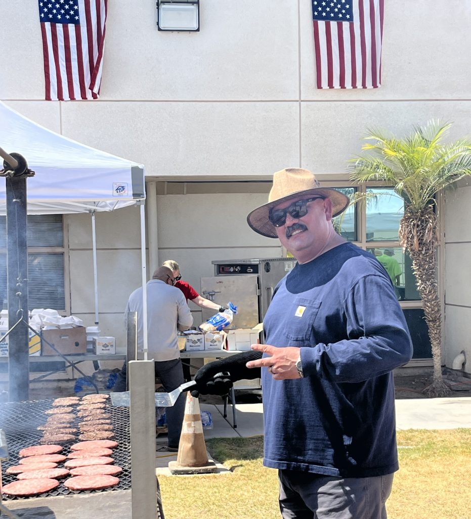 A Calipatria State Prison leader works the grill during the staff appreciation event held July 1, 2026. US flags hang along the Administration Building.