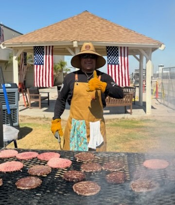 Giving a thumbs up, a man wearing a large apron works the grill.