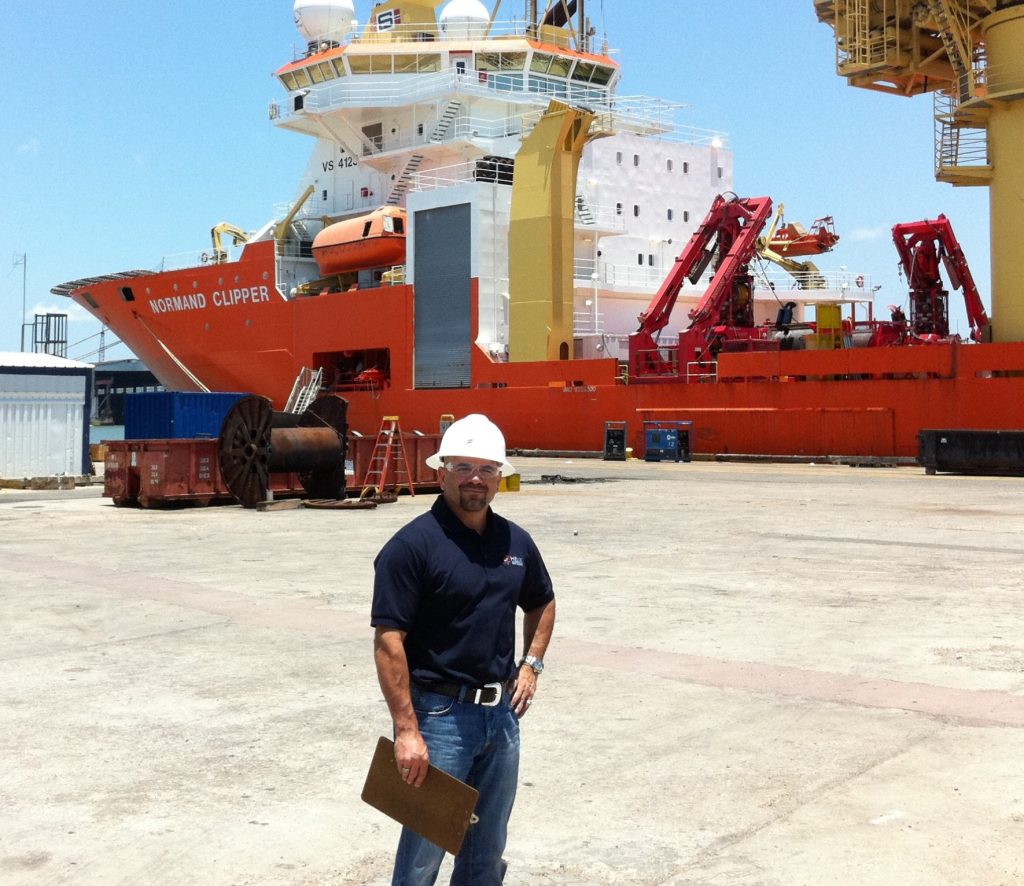 David Tucker on a dock with a large commercial ship behind him. 