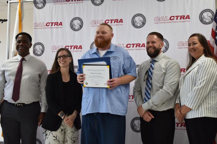 Incarcerated graduate smiles in group photo at ceremony for program completion