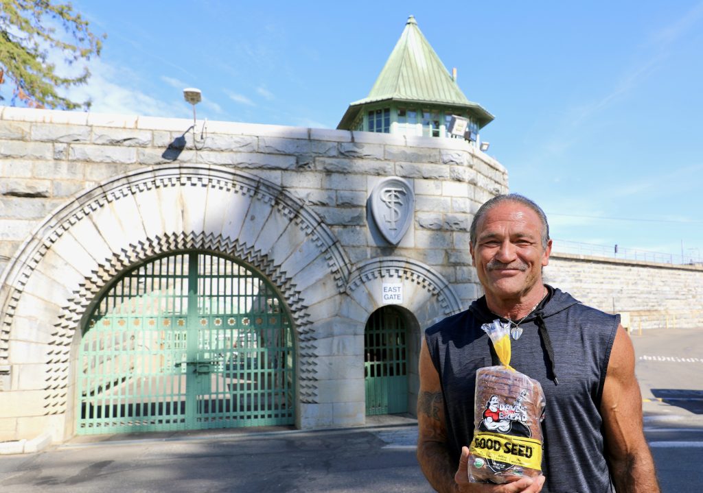 Dave Dahl with a loaf of the bread he helped create standing in front of Folsom State Prison.