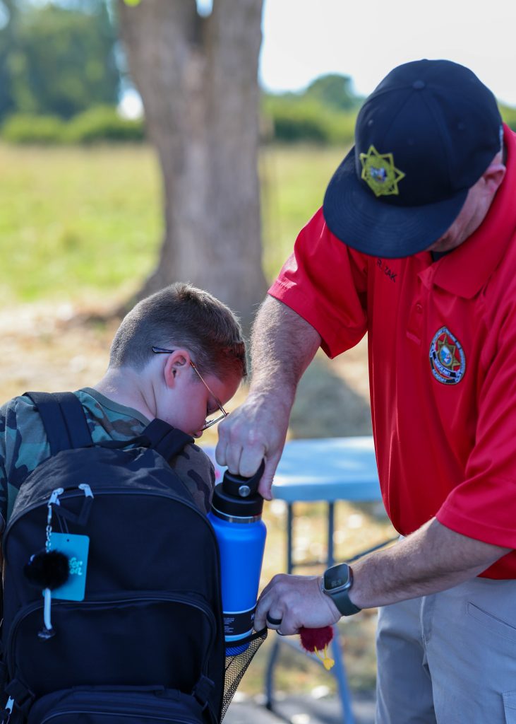 CDCR Academy staff helps a child adjust a backpack and places a water bottle in a side pocket.
