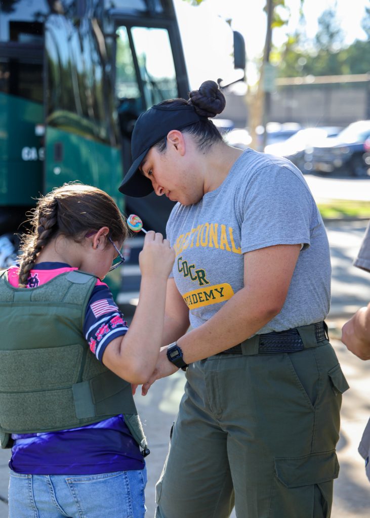 Cadet works with a child to try on a safety vest at the CDCR booth in Galt during National Night Out.