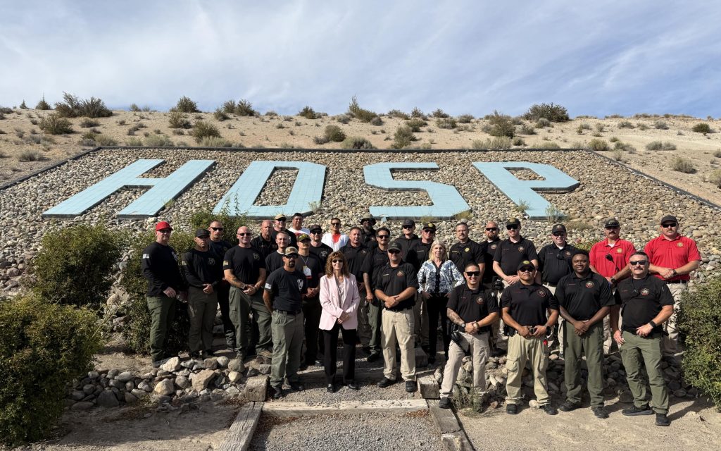 A group photo of staff at High Desert State Prison in Susanville as they stand before giant HDSP letters on a hillside.