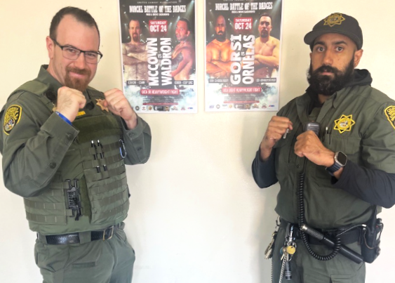 McCowan and Gorsi pose with fists up in front of their Battle of the Badges event posters