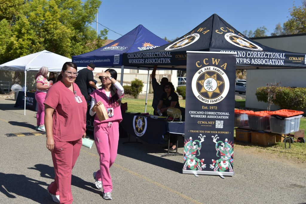 Staff members wearing pink scrubs walk by a booth at Avenal State Prison.