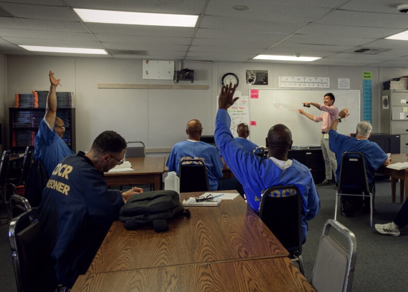 Incarcerated students with hands raised in institutional classroom