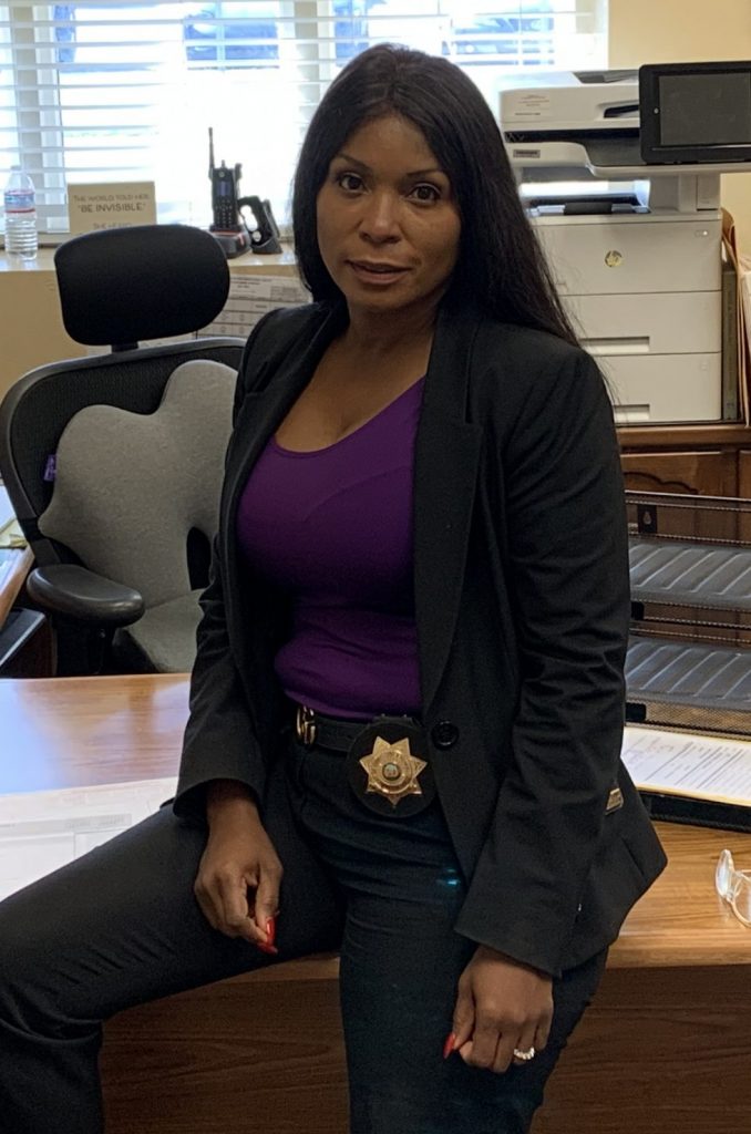 Woman wearing badge sits on her desk.