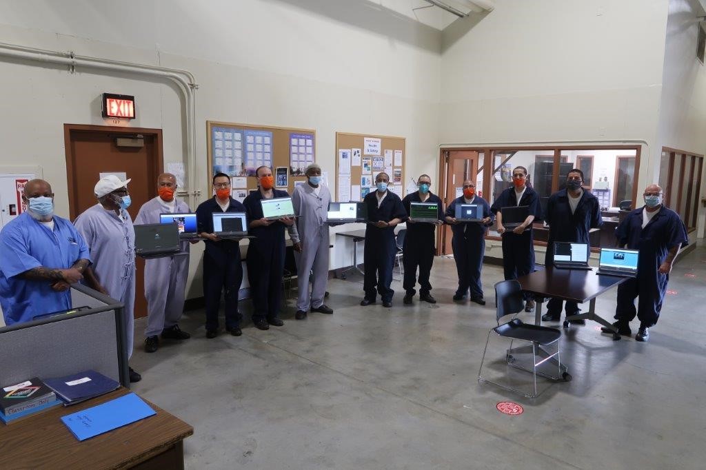 A dozen inmates holding laptops who are a part of the California Prison Launch Revolutionary Laptop Program.