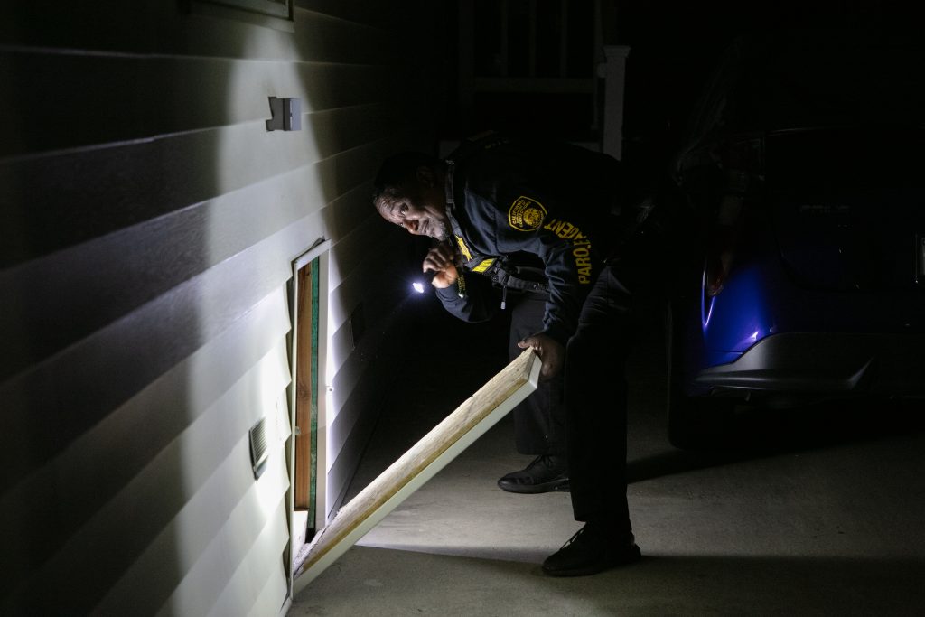 A parole agent using a flashlight to search a crawlspace under a parolee's home