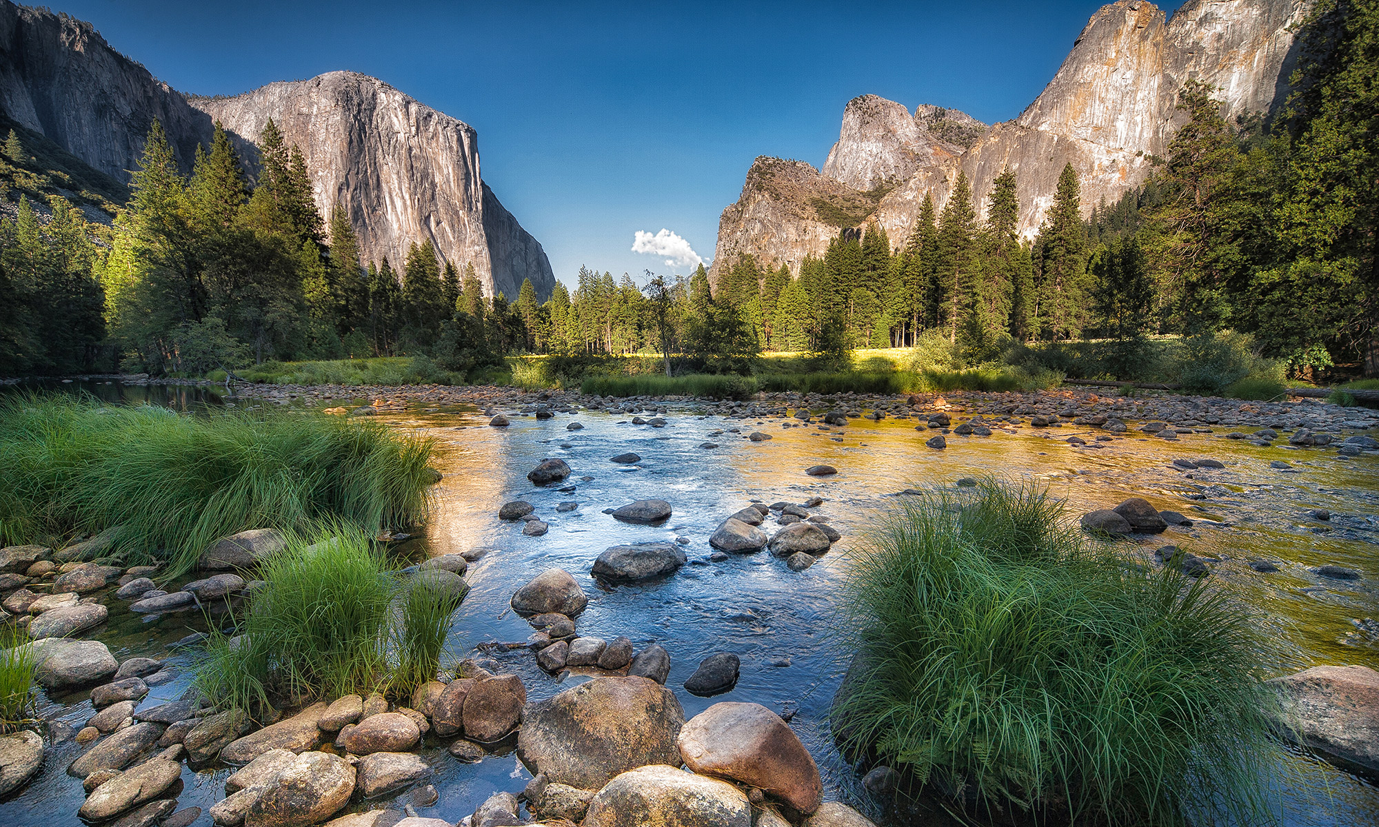 Yosemite National park with rocks, shallow lake and large rock mountain in the background in clear sky.