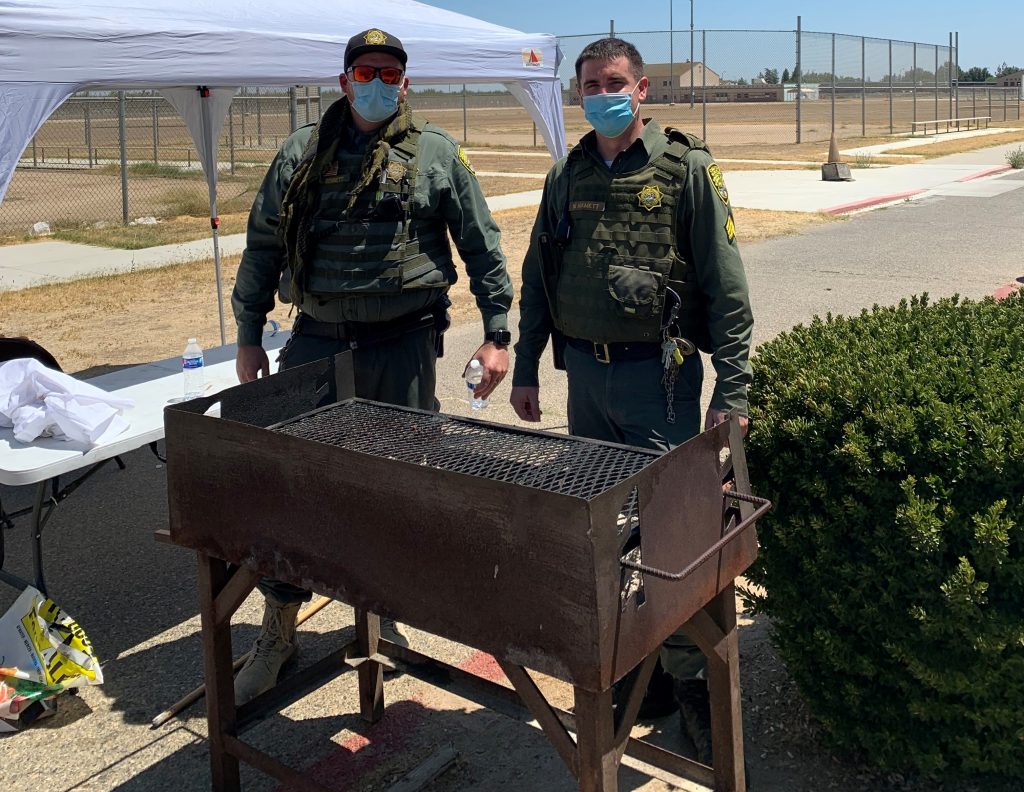 Two officers wearing procedure masks stand at a barbecue