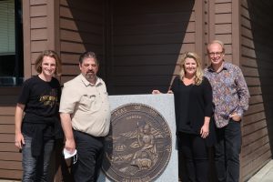 Four people stand in front of the California State Seal.