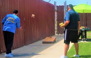 Two men, one incarcerated, play cornhole. Their backs are to the camera.
