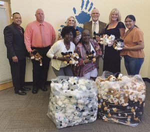 A group of people stand with two large clear bags full of stuffed dogs.
