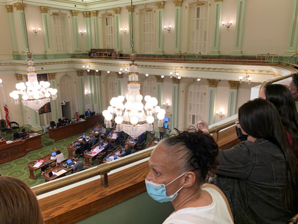 Women in masks sit in the balcony while lawmakers work on the floor below.