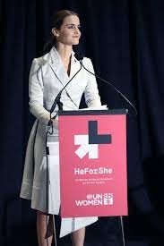 A woman wearing a white suit stands at a lectern