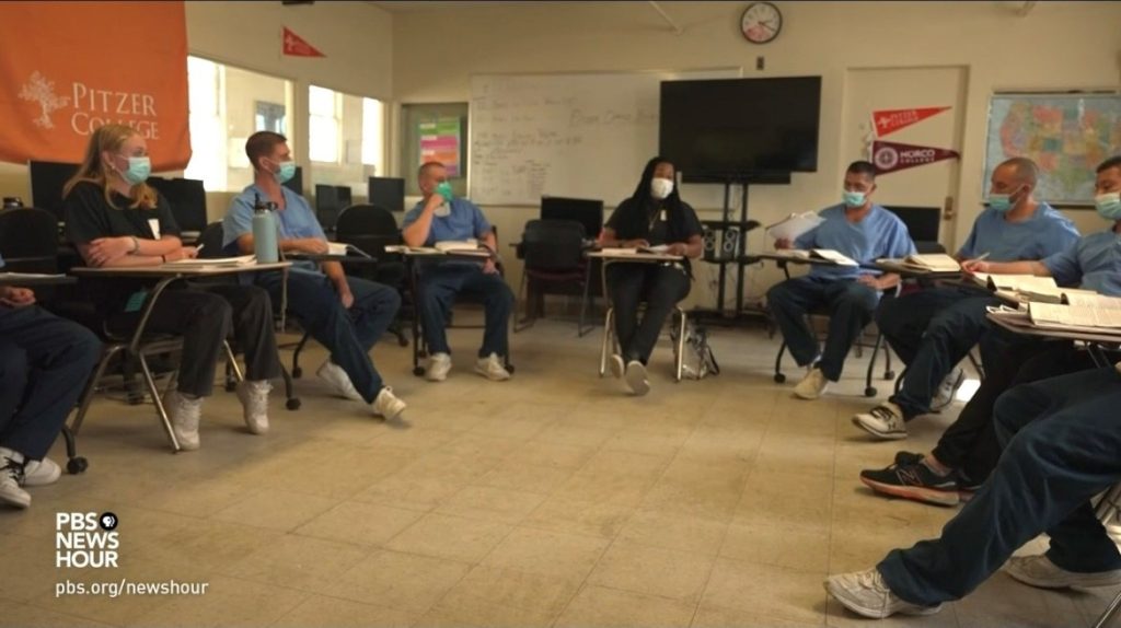 Incarcerated people wearing masks sit at desks in a classroom