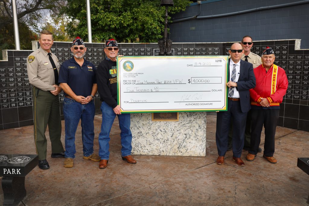 Six people at a veterans memorial holding a $4,000 check.