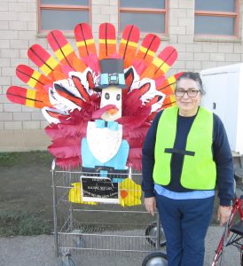 A woman in a hi-viz vest stands in front of a big turkey made out of colorful paper