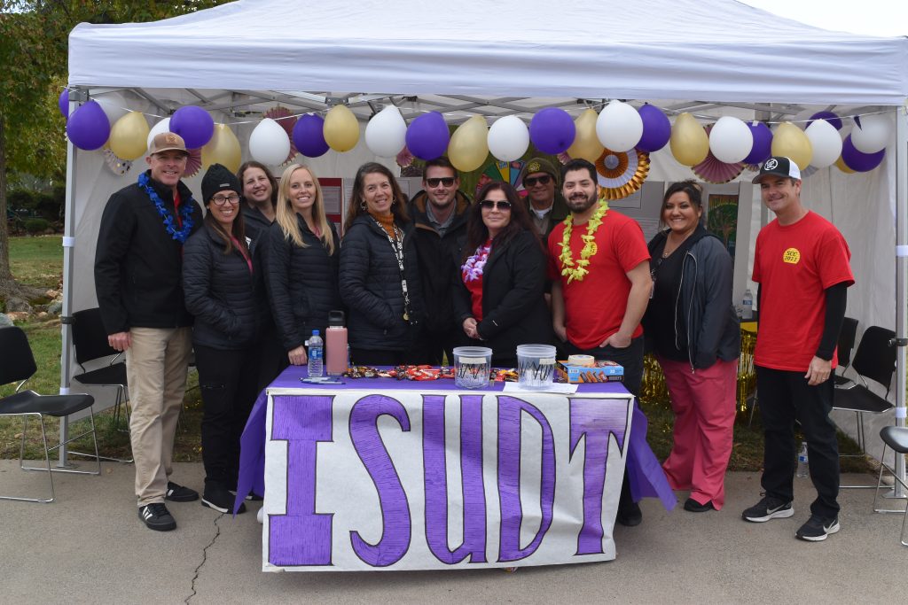 A group of people at a booth decorated with balloons that reads "ISUDT"