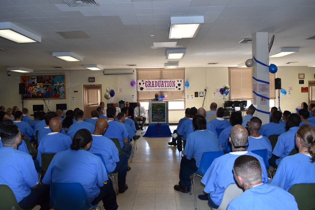 Incarcerated people listen to a guest speaker in a gym.