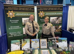 A man and woman in correctional officer uniforms at a hiring booth.