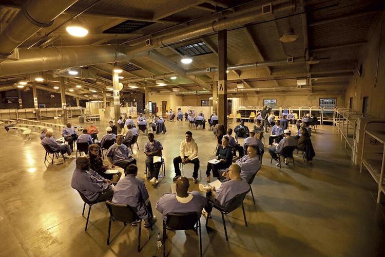 Incarcerated people sit in groups in a prison housing unit.