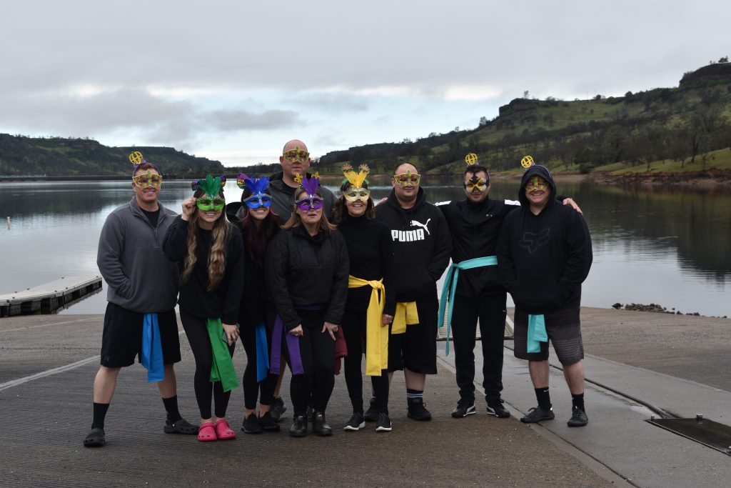 A group of people wearing Mardi Gras attire stand in front of a lake.