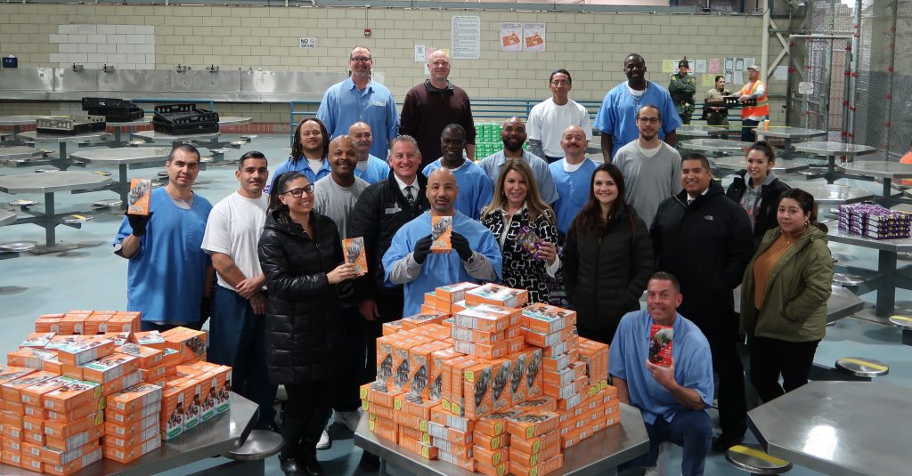 A group of incarcerated people and free staff in a prison cafeteria with Girl Scout cookie boxes piled on tables