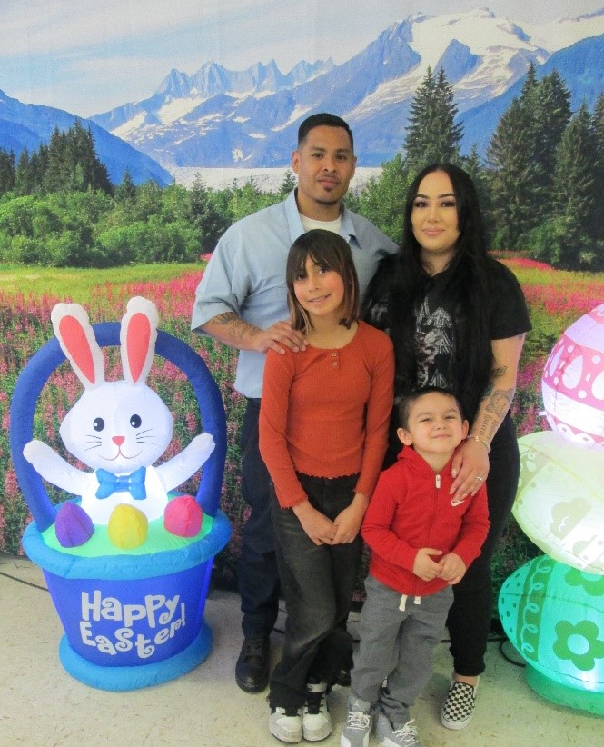 A family of four poses next to an Easter basket