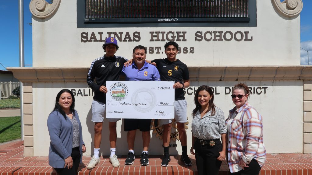 A group of people stands at a sign that says "Salinas High School." They are holding an oversized check.