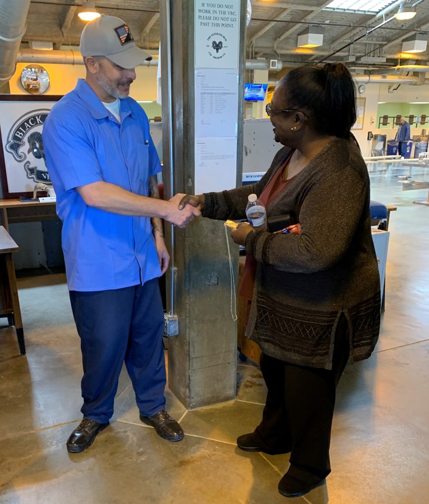 A woman in a sweater shakes hands with an incarcerated man.