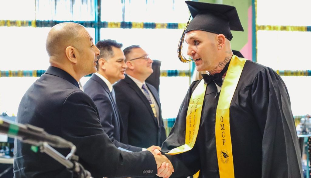 A man in a cap and gown shakes the hand of a man in a suit at a graduation