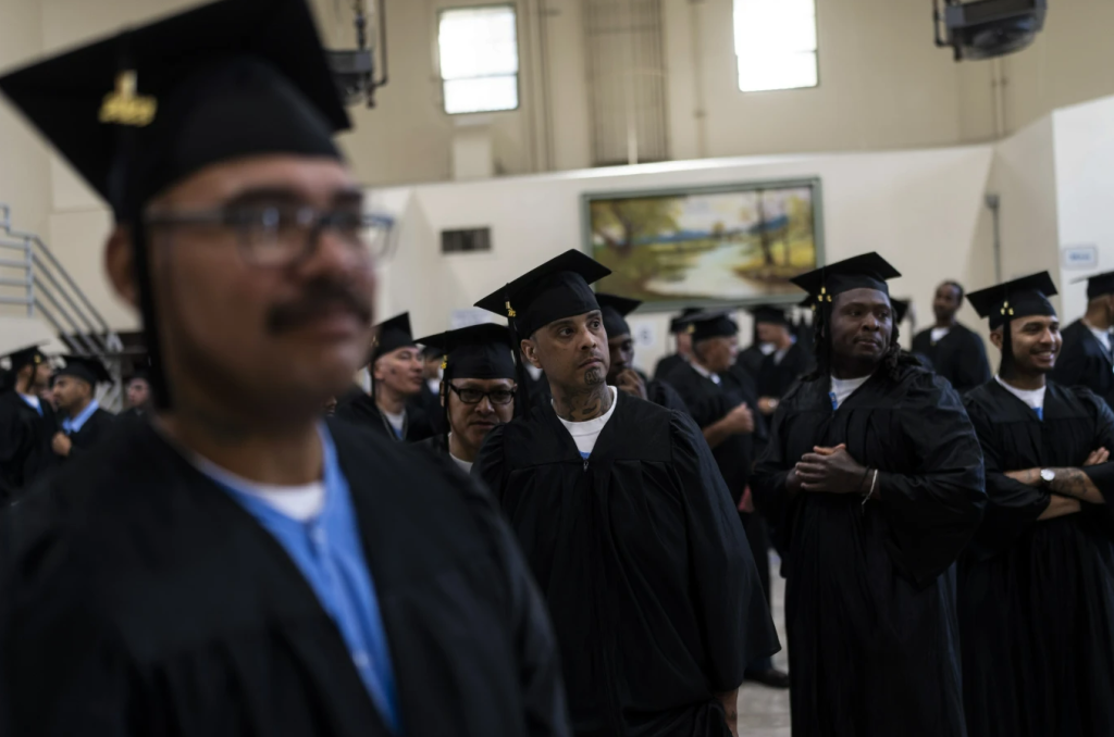 Men in graduation caps and gowns in a prison gymnasium.