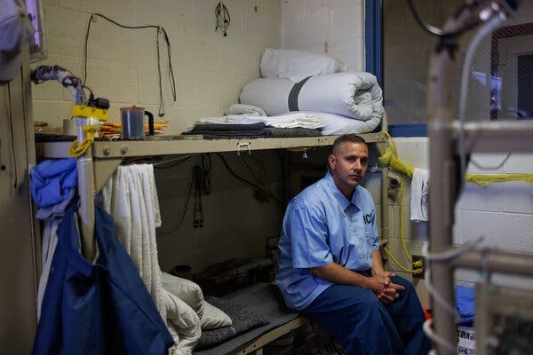 A man sits on the bottom bunk in a prison cell.