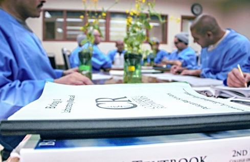 Incarcerated students sit at a desk covered with textbooks