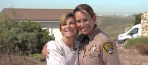 A woman in a white shirt and a woman in a correctional officer uniform have their arms around one another.