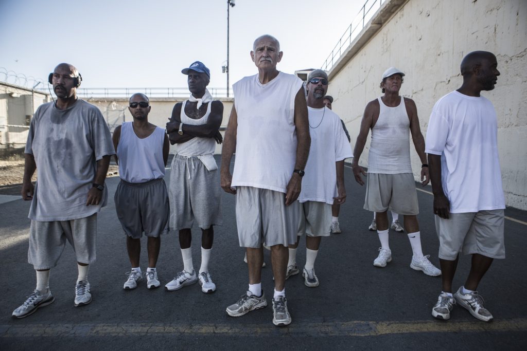 Seven men stand on a track on a prison yard.