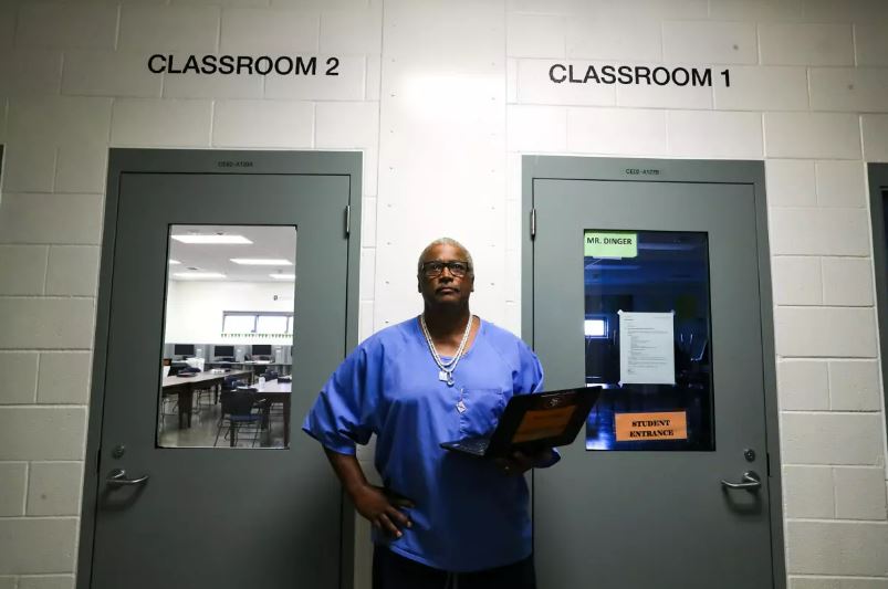 A man stands inside a prison holding a laptop