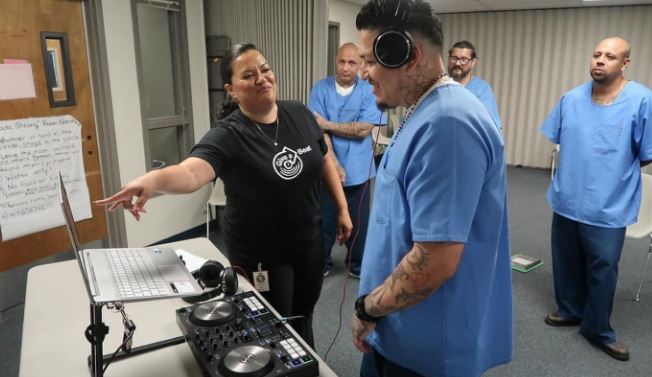 A woman points to a DJ system while incarcerated people watch