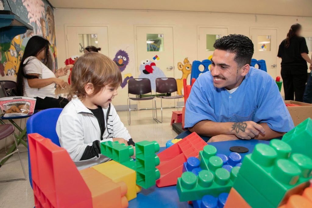 A man in a blue shirt plays with a child using large blocks
