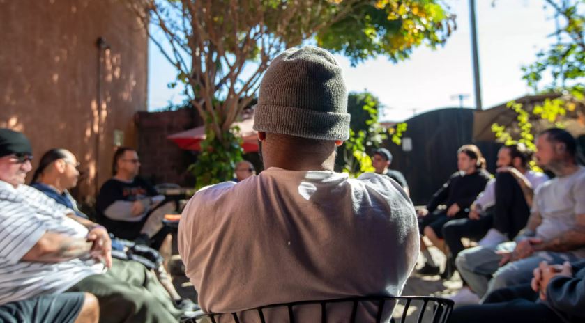 Back view of a man in a beanie talking to a group of people in a courtyard.