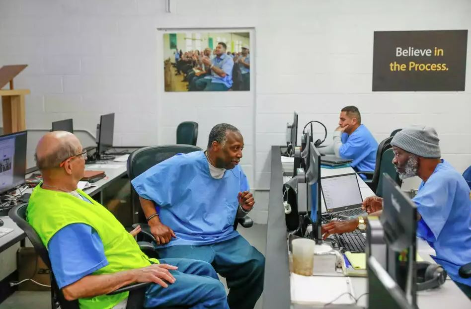 Incarcerated people talk while sitting at computers in a lab