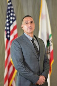 Photo of Acting Warden Leo Quiroz in front of US and California flags.